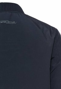 Marineblauwe jas met een hoge kraag, gemaakt van gladde stof; bevat een discreet logo op de achterkant en minimale stikseldetails.
