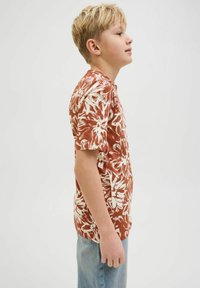 Camisa de manga corta en óxido con patrón floral blanco, cuello redondo, corte relajado y tejido ligero; combinada con jeans de color azul claro.