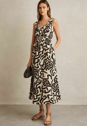 Maxi šaty v krémovej farbe s čiernymi abstraktnými vzormi, s volánovým výstrihom, elastickým pásom a bočnými vreckami. Skombinované s hnedými sandálmi.