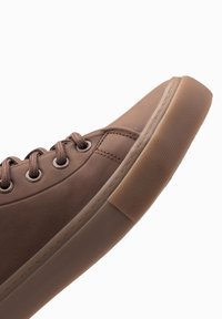 Zapatilla de cuero marrón con punta redonda, suela de goma texturizada, ojales de metal y cordones. Presenta un upper suave y una suela acolchada.
