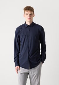 Camisa de manga larga azul marino oscura hecha de una tela suave, con un cierre de botones en la parte delantera y un dobladillo ligeramente curvado, combinada con pantalones gris claro.