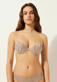 Metallisk beige bikiniöverdel med bygel, veckade kupor och tunna justerbara band. Tyget har en glittrande textur och mjuk yta.