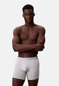Męskie boxery Calvin Klein w jasnoszarym kolorze, wykonane z bawełny, z miękkim paskiem wytłaczanym logo, dopasowanym krojem oraz gładką fakturą.