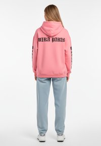 Felpa rosa con "MIRA PARIS" in nero sulla parte posteriore, abbinata a pantaloni della tuta blu chiaro. Tessuto morbido con un taglio rilassato e design con cappuccio.