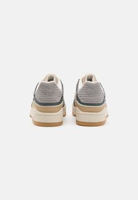 Vue arrière de baskets gris et beige avec une finition en daim texturé, une épaisse semelle crème et une semelle en caoutchouc brun, comportant un détail de logo sur le talon.