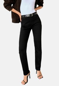 Melnas džinsu bikses ar šauru piegriezumu, augstu jostasvietu un piecu kabatu dizainu, kombinētas ar melnu ādas jostu un atvērtā purngalā augstpapēžu kurpēm.