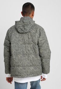 Kurtka z ociepleniem i kapturem, ozdobiona zielono-czarnym wzorem zwierzęcym, o miękkiej teksturze i elastycznych mankietach. Widoczne detale przeszyć.