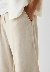 Licht beige linnen broek met een relaxte pasvorm, zichtbare zijzakken en een subtiele textuur. Heeft een losse zoom voor comfort en ademend vermogen.