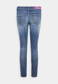 Jeans skinny blu sbiaditi con due tasche posteriori e una patch floreale rosa sulla cintura, su uno sfondo bianco.