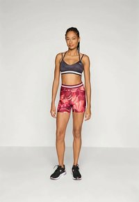 Sujetador deportivo negro con rayas blancas, pantalones cortos con estampado floral rosa y zapatillas negras. Tejido suave, diseño ajustado y cintura media.