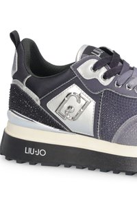 Donkergrijze en zwarte sneaker met zilveren accenten, getextureerde panelen, zwarte veters en "LIU·JO" branding op de zool en zijlogo.