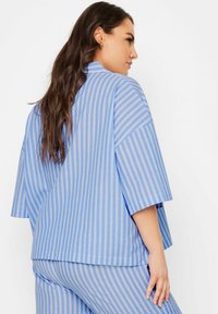 Blårandig oversized topp med korta ärmar, featuring en rund halsringning och en avslappnad passform, tillverkad av ett lättviktigt bomullsmaterial.