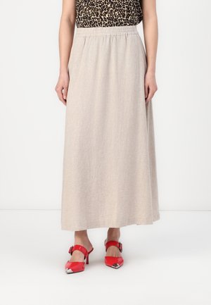 Femme portant une longue jupe beige à taille élastique, un haut à imprimé léopard, et des mules à talons rouges avec des embouts argentés.