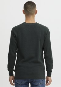 Pulover din tricot cu nervuri de culoare verde închis, cu mâneci lungi, gât rotund și mansete și tiv cu nervuri. Are un design cu mânecă raglan și o textură subtilă.