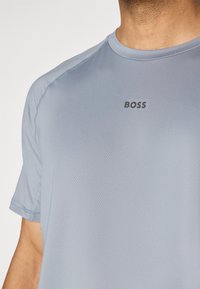Lys blå kortermet t-skjorte laget av glatt stoff, med logoen "BOSS" i mørkegrått på brystet. Sømdetaljer synlige.