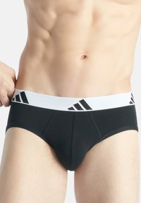 Slip neri in materiale morbido con vita elastica bianca che presenta righe nere e dettagli del logo.