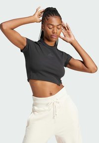 Black cropped t-shirt with ribbed texture and short sleeves, featuring a small logo on the chest. Paired with high-waisted white sweatpants.