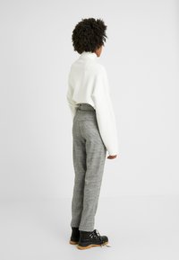White turtleneck sweater, gray plaid trousers, and black lace-up boots with a rubber sole. The outfit has a relaxed fit and tailored silhouette.