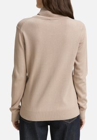Pull-over beige en maille douce, muni d'un design ajusté, de accents côtelés aux poignets et à l'ourlet, ainsi qu'un dos sans couture.