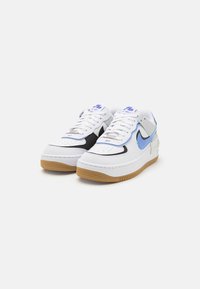 Bílé kožené tenisky s černými a světle modrými akcenty. Mají texturovanou gumovou podrážku a perforovanou špičku. Šňůrky a značení jsou modré.