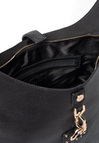 Černá texturovaná kožená kabelka s otevřeným zipem, ukazující hladký černý textilní interiér a vnitřní kapsu na zip. Viditelné detaily zlatého kování.