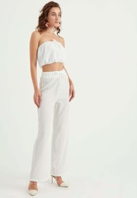 Vit avskuren strapless topp med knytdetalj, kombinerad med högmidjade vida byxor i texturerat tyg och nude klackskor.