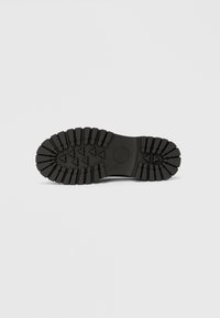 Čierna gumová podrážka topánky s hrubým dezénom s trojuholníkovými výstupkami pre lepšiu trakciu a hladkou stredovou časťou.