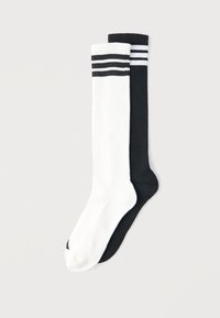 Ζευγάρι κάλτσες μέχρι το γόνατο με ριγέ ανάγλυφη υφή, μία λευκή με μαύρες ρίγες και μία μαύρη με λευκές ρίγες, απλωμένες σε φωτεινό φόντο.