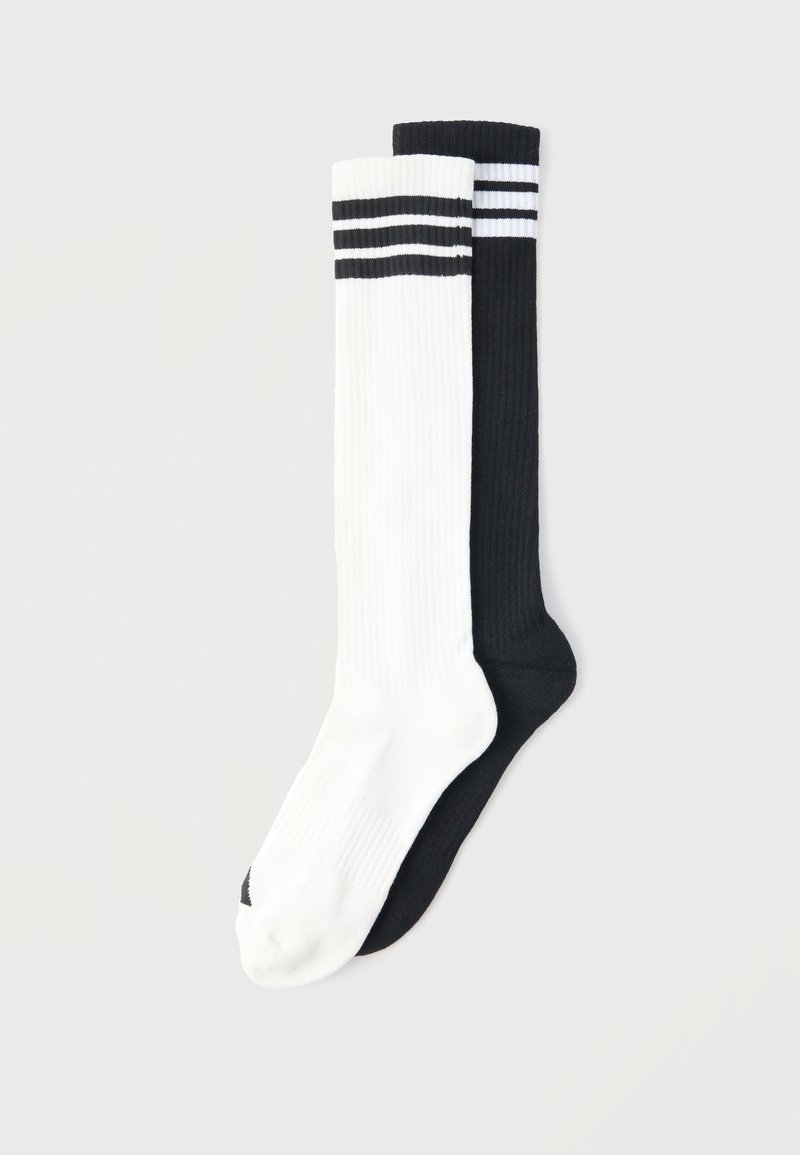 Ζευγάρι κάλτσες μέχρι το γόνατο με ριγέ ανάγλυφη υφή, μία λευκή με μαύρες ρίγες και μία μαύρη με λευκές ρίγες, απλωμένες σε φωτεινό φόντο.