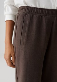 Braune, strukturierte Stoffhose mit elastischem Bund und seitlicher Tasche, mit lockerem Schnitt und minimalistischen Designdetails.