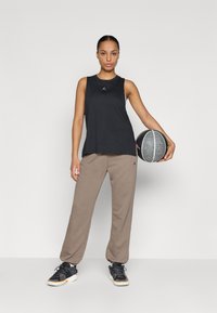 Svart ermeløs treningsgenser, beige smale joggebukser og svarte joggesko med hvite detaljer. Holder en sort og hvit basketball.