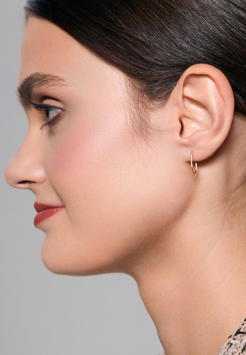 Złote geometryczne kolczyki w formie obręczy o kanciastym wzorze, noszone na lewym uchu. Gładka metalowa powierzchnia i minimalistyczne cechy.