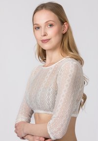 Weißes Spitzen-Crop-Top mit langen Ärmeln, gewelltem Saum und filigranen Musterdetails. Weicher, transparenter Stoff mit strukturierten Verzierungen.