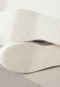 White rubber shoe soles featuring a textured surface with geometric patterns and the word "NEXT" repeated throughout. Smooth edges.