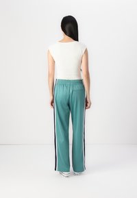 En tettsittende hvit ermeløs topp kombinert med løse teal joggebukser med marineblå sidestreker og baklomme. Sneakers fullfører looken.