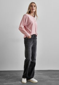 Haut rose clair à manches longues avec une coupe décontractée, associé à un jean large gris foncé et des baskets blanches. Design simple, accents minimaux.