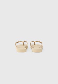 Tan flip-flops with textured footbed and gold-tone straps, featuring a minimalist design and flat sole, viewed from the back.