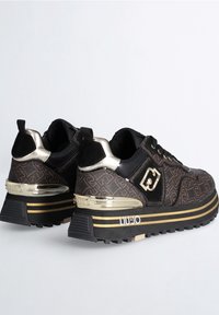 Baskets compensées à motif noir et marron avec des accents dorés, des semelles texturées et des détails de logo sur les côtés et les talons.