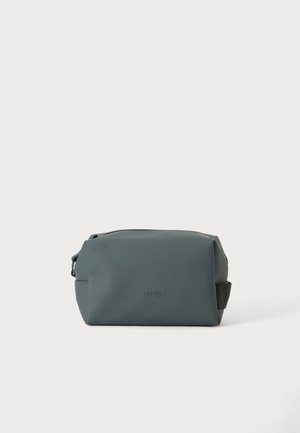 Trousse de toilette rectangulaire gris foncé avec fermeture éclair et nom de marque discrètement embossé sur le devant sur fond uni.