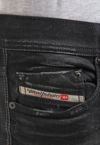 Close-up of black denim jeans back pocket with a Diesel Industry fabric label sewn inside.