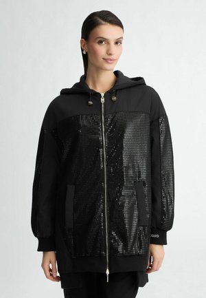 Black hooded jacket featuring a sequined front panel, zip closure, and pockets. Made from smooth fabric, with ribbed cuffs and hem.