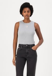 Grå ribbestrikket tank topp med ermeløst design, med en liten CK-logo på brystet, sammen med høyt liv svarte denim jeans.
