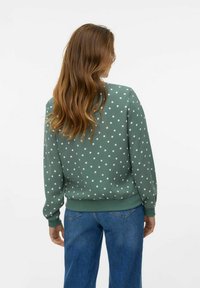 Sweatshirt vert à pois avec une coupe décontractée, col et poignets côtelés. Associé à un jean bleu taille haute. Texture lisse sur l'ensemble.