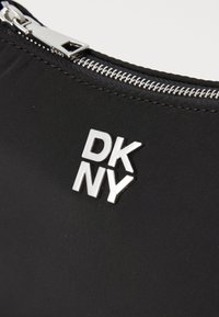 Materiale in nylon nero con zip argentata e logo DKNY. La texture è liscia, con un design minimalista privo di ulteriori motivi.
