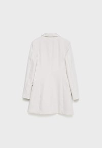 Blazer blanc à manches longues avec col, présenté de dos, doté d'une coupe ajustée et de détails sur les coutures latérales.