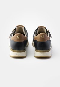 Černé kožené tenisky s hnědými akcenty, texturovaným zadním dílem, bílou podrážkou, bočními zipy a vyraženým logem na patě. Filtr pozadí v odstínech šedi.