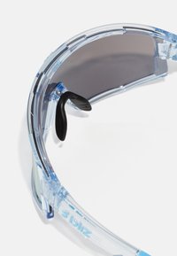 Ochelari de soare sport clare cu ramă transparentă și lentile gri. Include tampoane negre pentru nas și branding embosat pe templu.