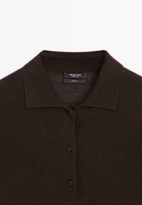 Brauner Woll-Polohemd mit klassischem Kragen, Knopfleiste und glattem Textur. Das Etikett weist auf eine Zusammensetzung von 100 % Wolle hin.