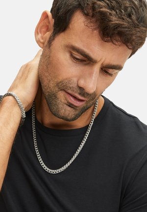 Silver chain necklace, thick links, worn over a black t-shirt. Bracelet matches necklace, smooth texture, looped design, reflective finish.