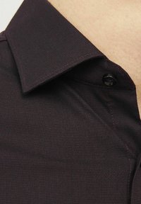 Tamno ljubičasta teksturirana košulja s ovratnikom i detaljem gumba. Tkanina ima finu strukturu koja prikazuje suptilni sjaj i glatku površinu.